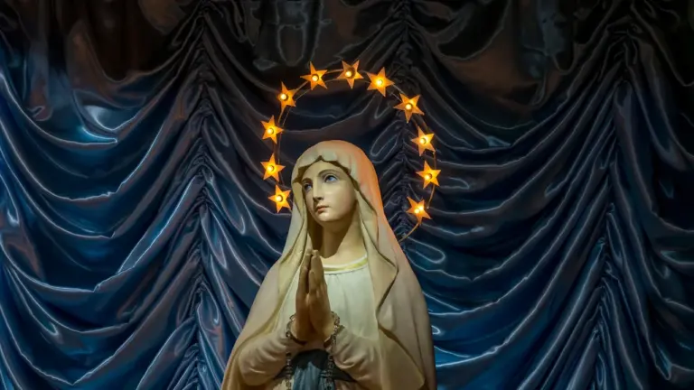 Eine leuchtende Marienfigur mit Sternenkranz vor einem blauen Vorhang zur Feier von Mariä Himmelfahrt.