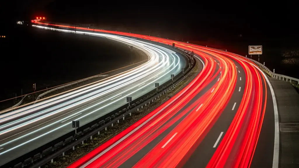 Langzeitbelichtung einer deutschen Autobahn bei Nacht mit hellen Lichtspuren der Fahrzeuge.