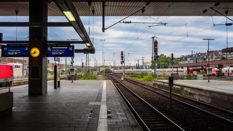 Moderner Bahnsteig mit Gleisen und Oberleitungen an einem deutschen Bahnhof bei Tageslicht.