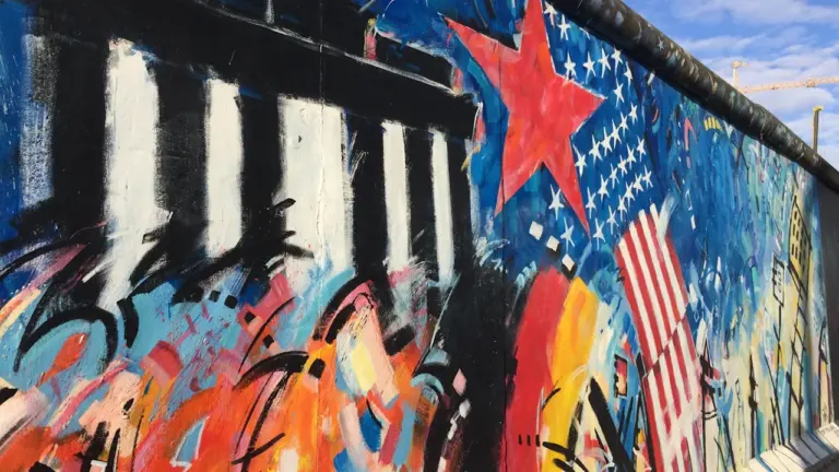 Die Berliner Mauer mit künstlerischem Graffiti und symbolischen Motiven vor blauem Himmel.