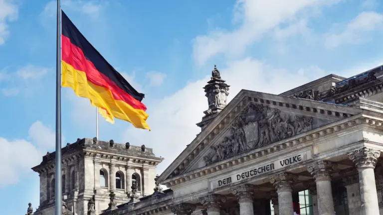 Die deutsche Flagge weht vor dem Berliner Reichstagsgebäude unter blauem Himmel.