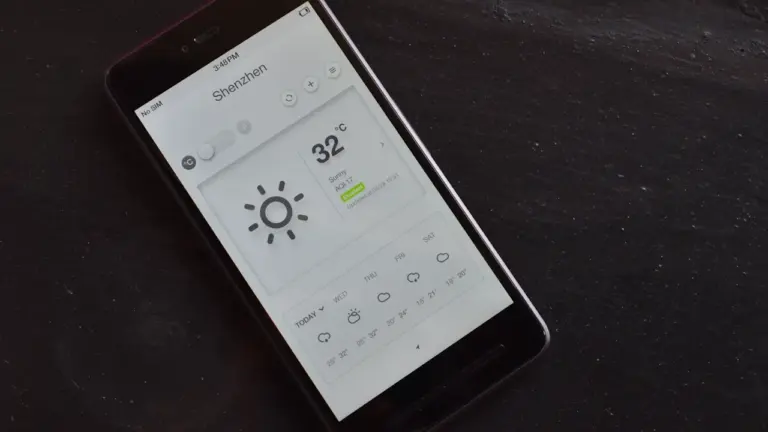 Ein Smartphone zeigt eine Wettervorhersage mit Temperaturen und Sonnensymbol auf dem Display.