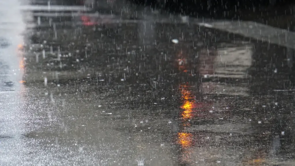 Eine regnerische Straße mit Reflexionen und einem roten Ampelsignal bei schlechtem Wetter.