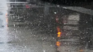 Eine regnerische Straße mit Reflexionen und einem roten Ampelsignal bei schlechtem Wetter.