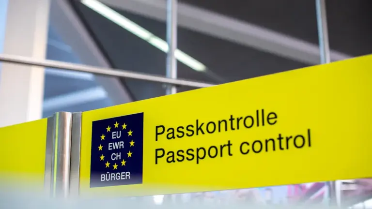 Ein gelbes Hinweisschild zur Passkontrolle an einem europäischen Flughafen für Reisende.