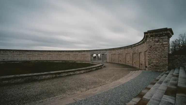 Die Gedenkstätte Buchenwald mit der markanten geschwungenen Steinmauer unter einem bewölkten Himmel.