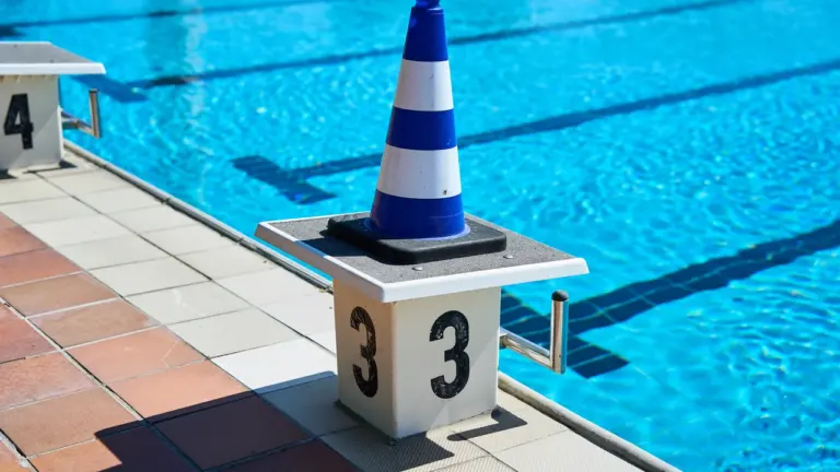 Ein blau-weiß gestreifter Pylon steht auf einem Startblock mit der Nummer Drei am Schwimmbecken.