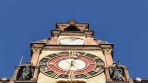 Ein historischer Uhrturm mit aufwendigen Verzierungen und zwei Engelfiguren vor einem tiefblauen Himmel.