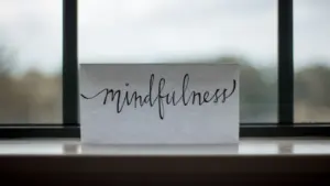 Ein Blatt Papier mit dem handgeschriebenen Wort Mindfulness vor einem Fenster.