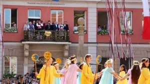 Kinder in bunten Kleidern führen vor einem historischen Gebäude einen traditionellen Tanz auf.