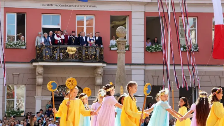 Kinder in bunten Kleidern führen vor einem historischen Gebäude einen traditionellen Tanz auf.