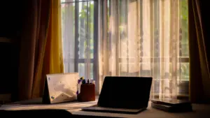 Ein Laptop steht morgens an einem Schreibtisch vor einem sonnendurchfluteten Fenster.