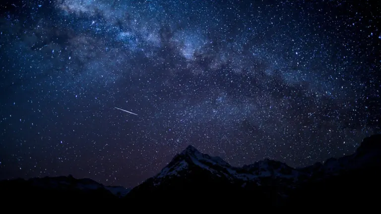 Sternschnuppe am nächtlichen Sternenhimmel über einem markanten Bergmassiv in der Dunkelheit.