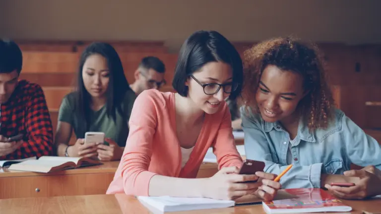 Schülerinnen in einem Klassenzimmer betrachten gemeinsam konzentriert einen Smartphone-Bildschirm für Unterrichtszwecke.