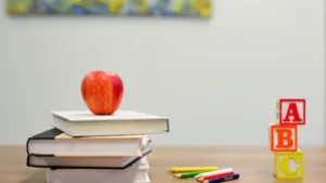 Ein roter Apfel liegt auf einem Stapel Schulbücher neben ABC-Holzwürfeln und Buntstiften.