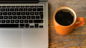 Laptop auf einem Schreibtisch neben einer Tasse schwarzem Kaffee bei der Büroarbeit.