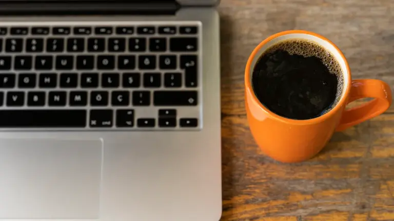 Laptop auf einem Schreibtisch neben einer Tasse schwarzem Kaffee bei der Büroarbeit.