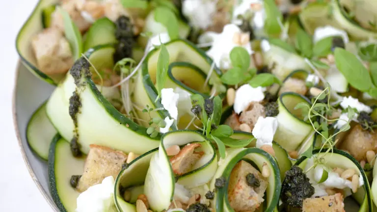 Ein köstlicher Zucchini-Salat mit Feta, Kräutern und Pinienkernen auf einem modernen Teller.