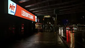 Ein beleuchteter Hit-Lebensmittelmarkt an einer nassen Straße bei Nacht in einer deutschen Stadt.