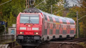 Ein roter Regionalzug der Deutschen Bahn fährt auf Gleisen durch eine grüne Landschaft.