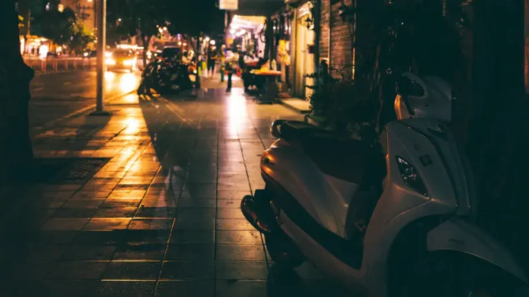 Ein einzelner E-Scooter steht nachts einsam am Straßenrand in der Stadt.
