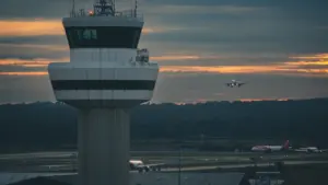 Fluglotsenturm am Flughafen Gatwick bei Dämmerung mit anfliegendem Flugzeug im Hintergrund