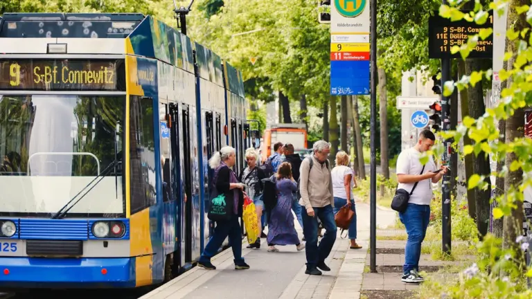 Menschen steigen an einer sonnigen Straßenbahnhaltestelle in eine moderne Bahn ein.