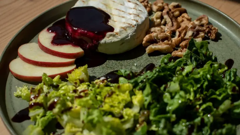 Gegrillter Ziegenkäse mit Walnüssen, frischem Feldsalat und Apfelscheiben auf einem Teller.