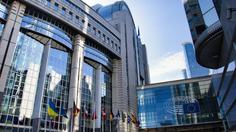 Das moderne Europaparlamentsgebäude mit verschiedenen Nationalflaggen vor einem klaren blauen Himmel.