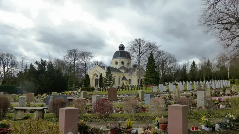 Ein friedlicher Sächsischer Friedhof mit einer Kuppelkirche und gepflegten Grabstätten bei bewölktem Himmel.